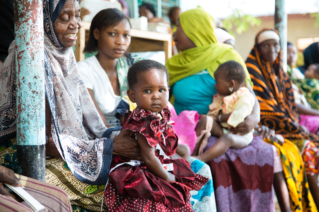 Families gather in the shade, layers of color and pattern moving through the frame.