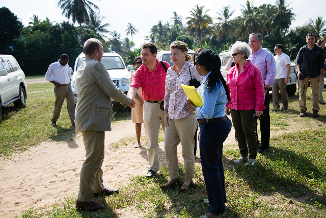 Introductions begin on a sunlit road, formal gestures softened by easy conversation.